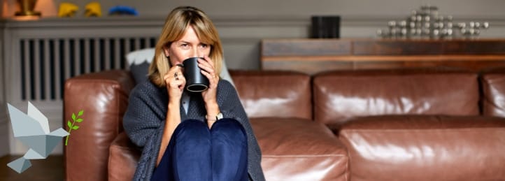 Woman sitting on couch wrapped in blanket drinking hot beverage, suggesting need for furnace repair or heating and air conditioning repair.
