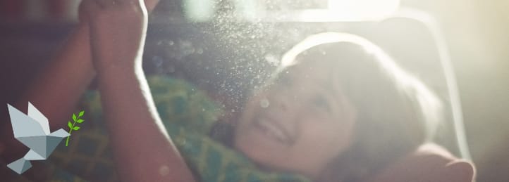 Smiling child lying in sunlight with visible dust particles, highlighting need for air duct cleaning.